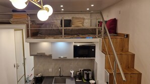 A compact studio apartment with a bunk bed, kitchenette, and a small bathroom.