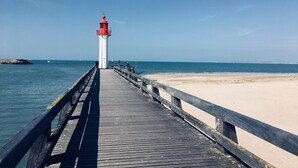 A wooden pier leading to a lighthouse with a red top, extending into a sandy beach area.