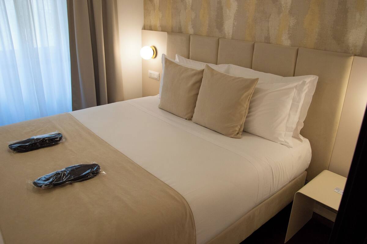 A neatly made bed with beige bedding, a headboard, and a bedside table with a lamp.