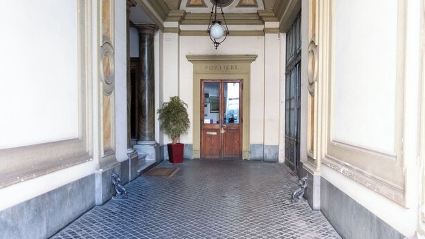 Ένας διάδρομος με πλακάκια στο δάπεδο, καμάρες στην οροφή και μια ξύλινη πόρτα με την επιγραφή «ΠΟΡΤΙΕΡΕ».