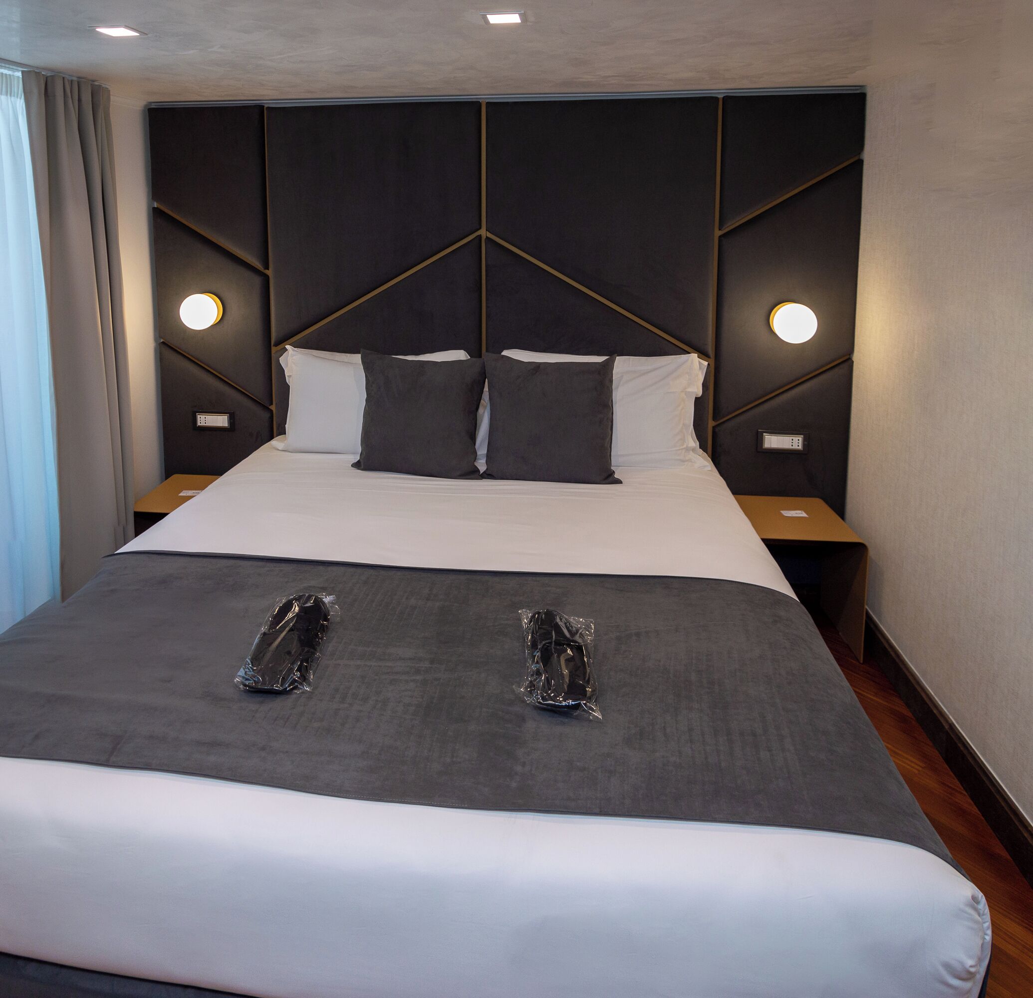 A modern hotel room with a large bed, two bedside tables, and a headboard with integrated lighting.