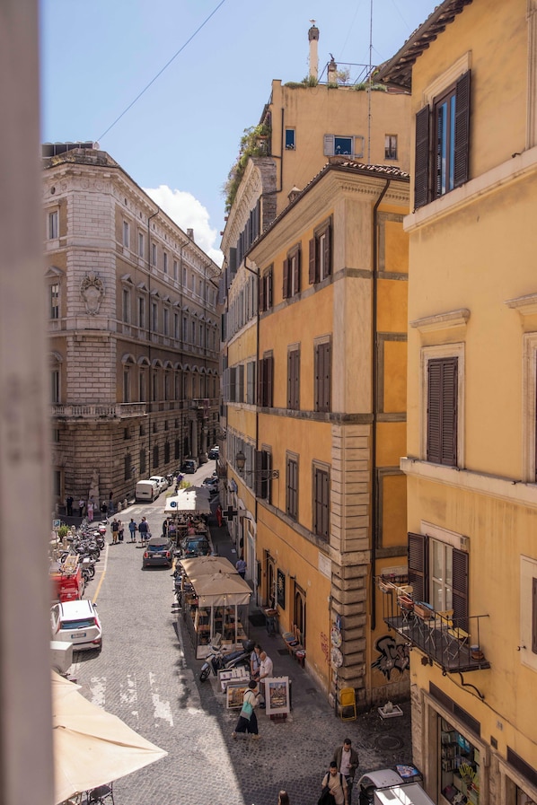 A narrow street with buildings on either side, a few parked cars, and a few people walking. - Home at Rome Luxury Navona Suites (Rome)