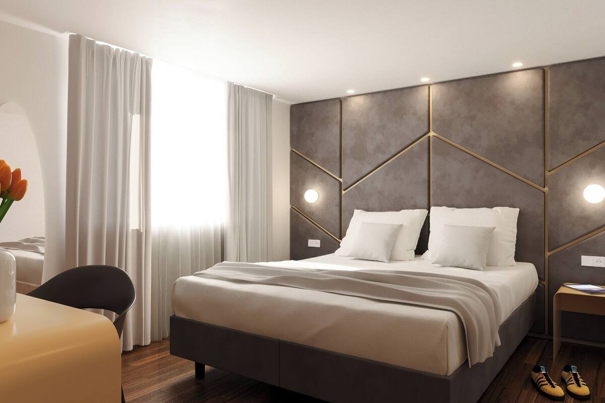 A modern bedroom with a large bed, a bedside table, a chair, and a desk with a vase of tulips.