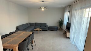 A modern living room with a wooden dining table, grey sofas, a small coffee table, a TV stand, and a potted plant. - Villa Moderne Avec Piscine Avignon (Avignon)