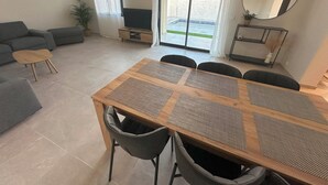 A modern living room with a wooden dining table, grey sofas, and a TV. - Villa Moderne Avec Piscine Avignon (Avignon)