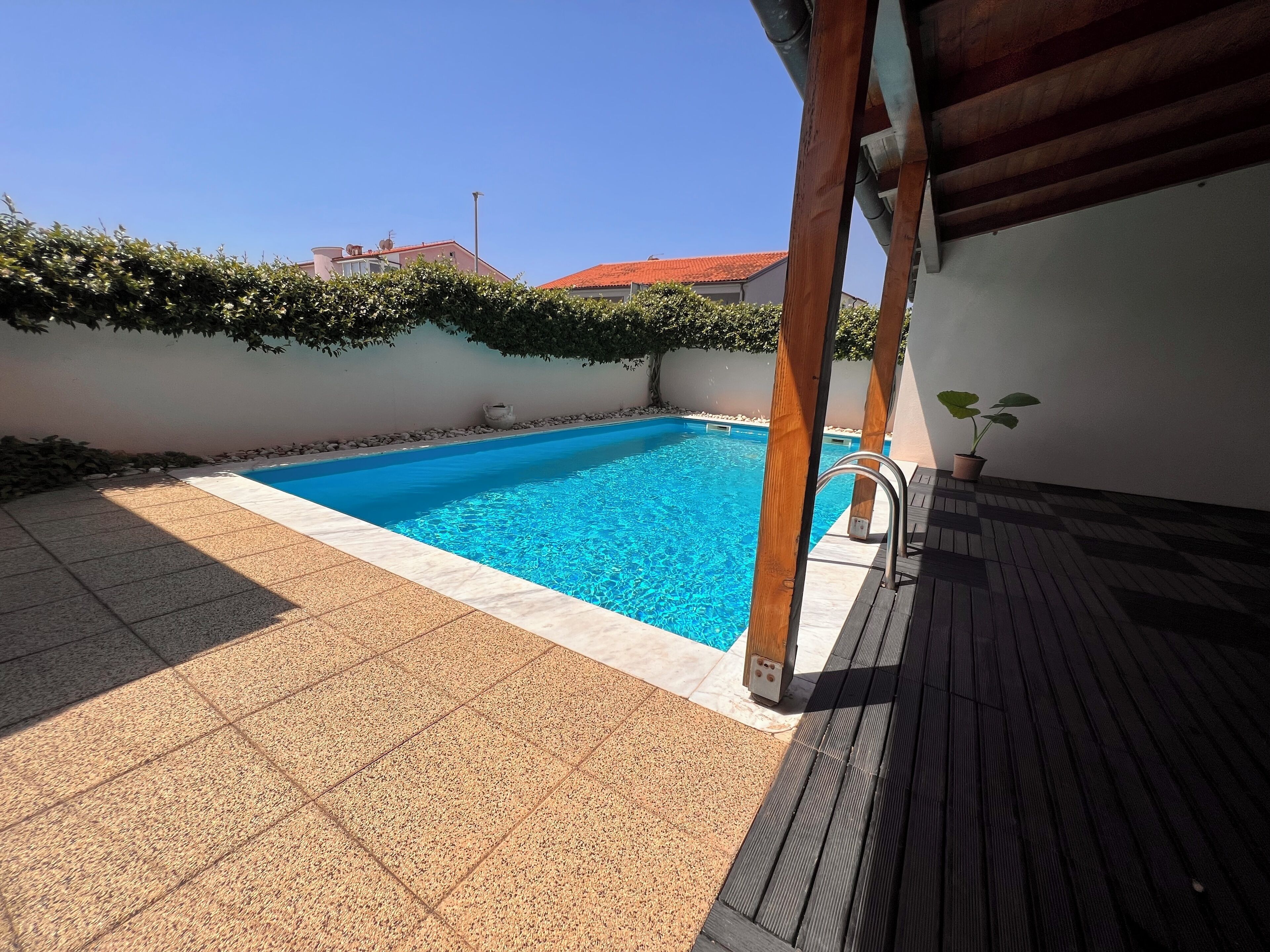 Une piscine rectangulaire à l’eau d’un bleu limpide, entourée d’une terrasse carrelée et d’une pergola en bois.
