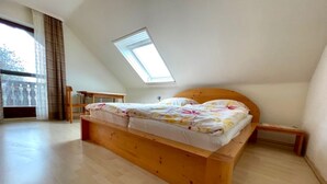 Une chambre avec un lit en bois, une lucarne et une vue sur l’extérieur.