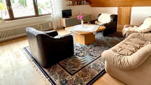 Un salon chaleureux avec un haut plafond en bois, une grande fenêtre, une cheminée et un coin salon confortable.