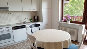 Une cuisine avec des meubles blancs, un lave-vaisselle, une cuisinière et une fenêtre donnant sur un paysage verdoyant.