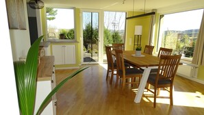 A dining area with a wooden table and chairs, a potted plant, and a view of greenery outside.