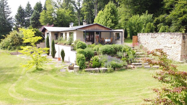 A house with a stone wall, a garden with various plants, and a lawn.