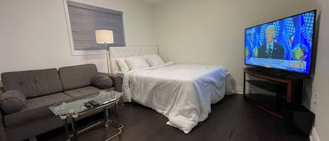 Una habitación de hotel con cama, sofá, mesa de centro de vidrio, televisor y lámpara.