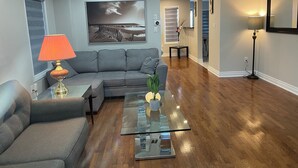 A modern living room with a grey sofa, a glass coffee table, and a lamp. - First Class - 2 bedroom house  (Whitby)
