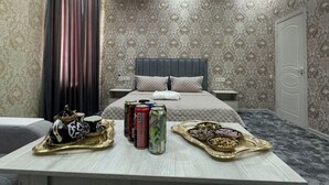 Habitación de hotel con cama, mesitas de noche, una bandeja con aperitivos y bebidas, y una cortina.