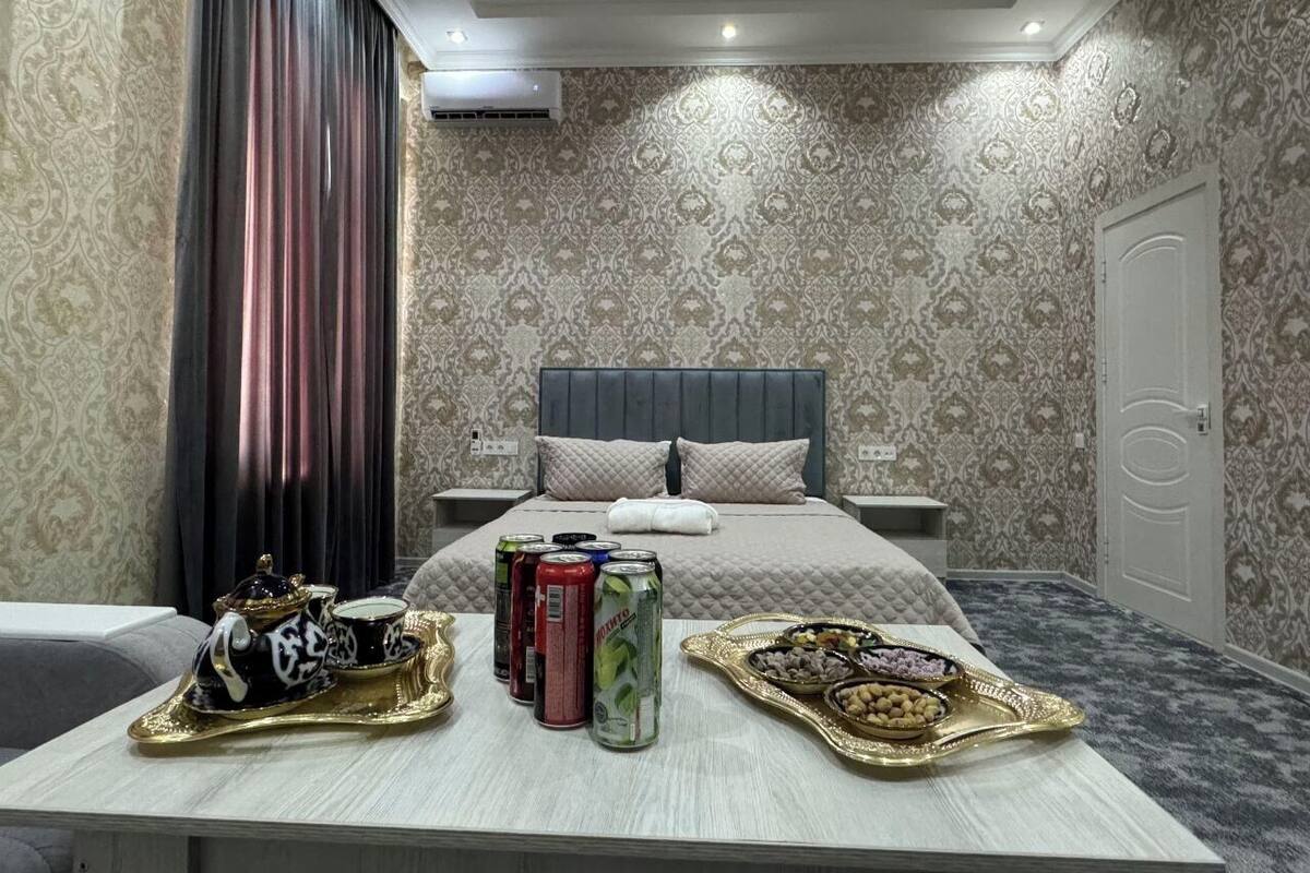 A hotel room with a bed, bedside tables, a tray with snacks and drinks, and a curtain.