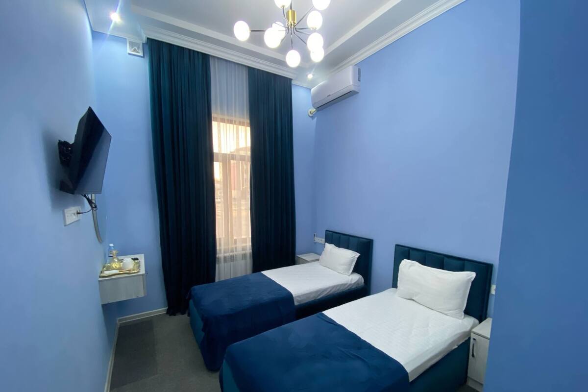 A hotel room with two beds, a TV, an air conditioner, and a window with curtains.