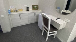 Una pequeña kitchenette con un refrigerador, una cafetera y un cuadro en la pared.
