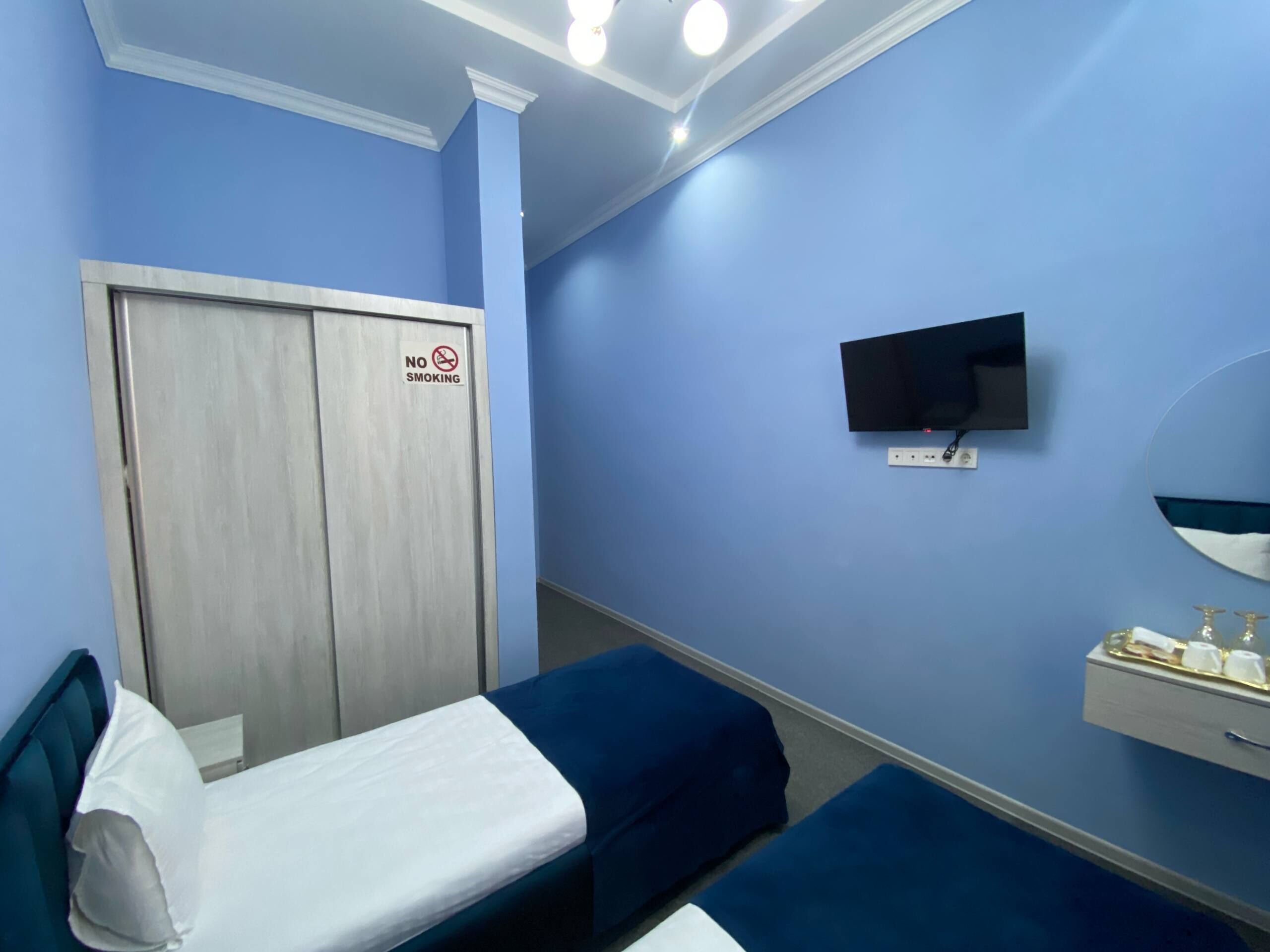 Une chambre d’hôtel équipée d’un lit, d’une télévision, d’un miroir, d’une armoire et d’un panneau indiquant « INTERDICTION DE FUMER ».
