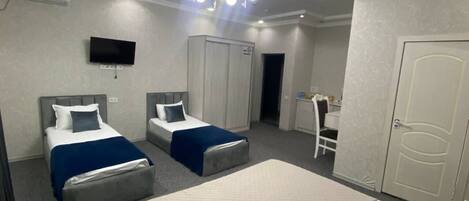 A hotel room with two beds, a television, a wardrobe, and a desk with a chair.