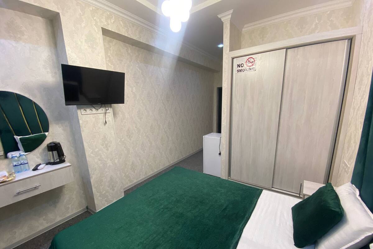 A hotel room with a bed, a TV, a desk with a mirror, a coffee maker, and a wardrobe with a 'No Smoking' sign.