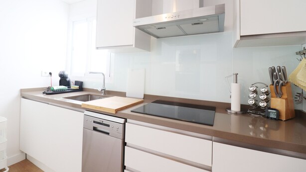 Une cuisine moderne avec des meubles blancs, un lave-vaisselle en acier inoxydable, une plaque de cuisson à induction noire et un bloc à couteaux.