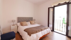 Une chambre à coucher comprenant un lit, des tables de chevet, une chaise et une porte-fenêtre coulissante donnant sur un balcon.