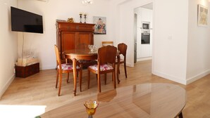 Un coin repas avec une table et des chaises en bois, un lustre et un téléviseur fixé au mur.