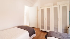 Une chambre avec deux lits, une armoire et une porte donnant sur une autre pièce.