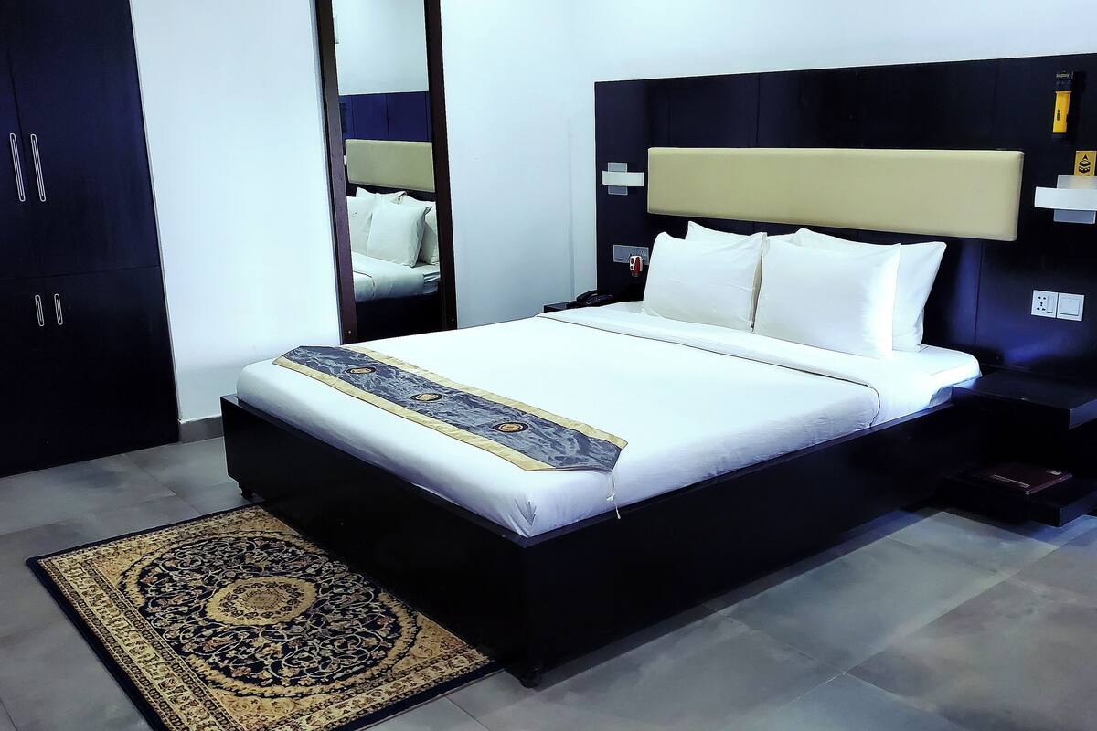 Una habitación de hotel moderna con una cama grande, una mesita de noche, un armario y un espejo.