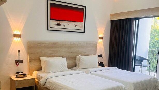 A modern hotel room with a large bed, bedside tables, a mounted artwork, and a view of the outdoors. - Kokomo Sunset Resort (Sreepur)