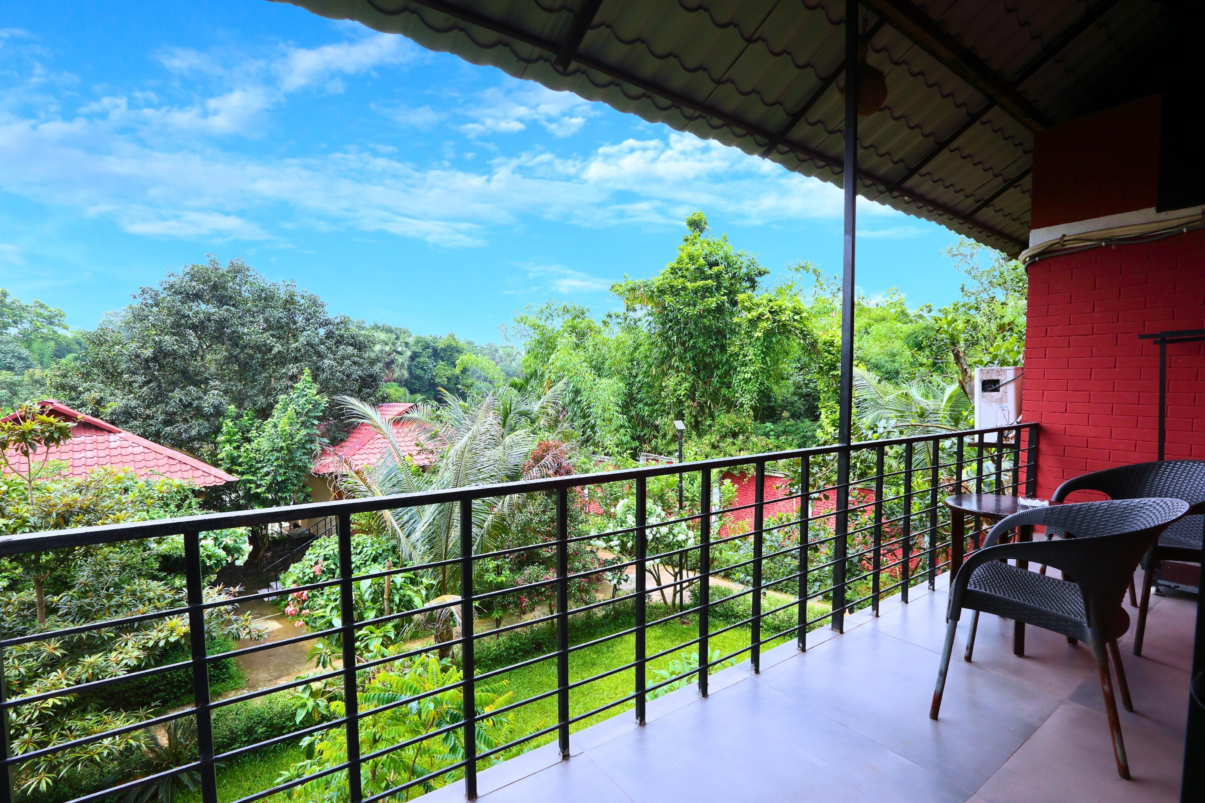 A balcony with a view of a lush garden and red-roofed buildings.