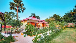 A two-story house with a red-tiled roof, surrounded by lush greenery and palm trees. - Kokomo Sunset Resort (Sreepur)