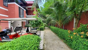 A red brick building with a covered walkway, a golf cart, and lush greenery. - Kokomo Sunset Resort (Sreepur)