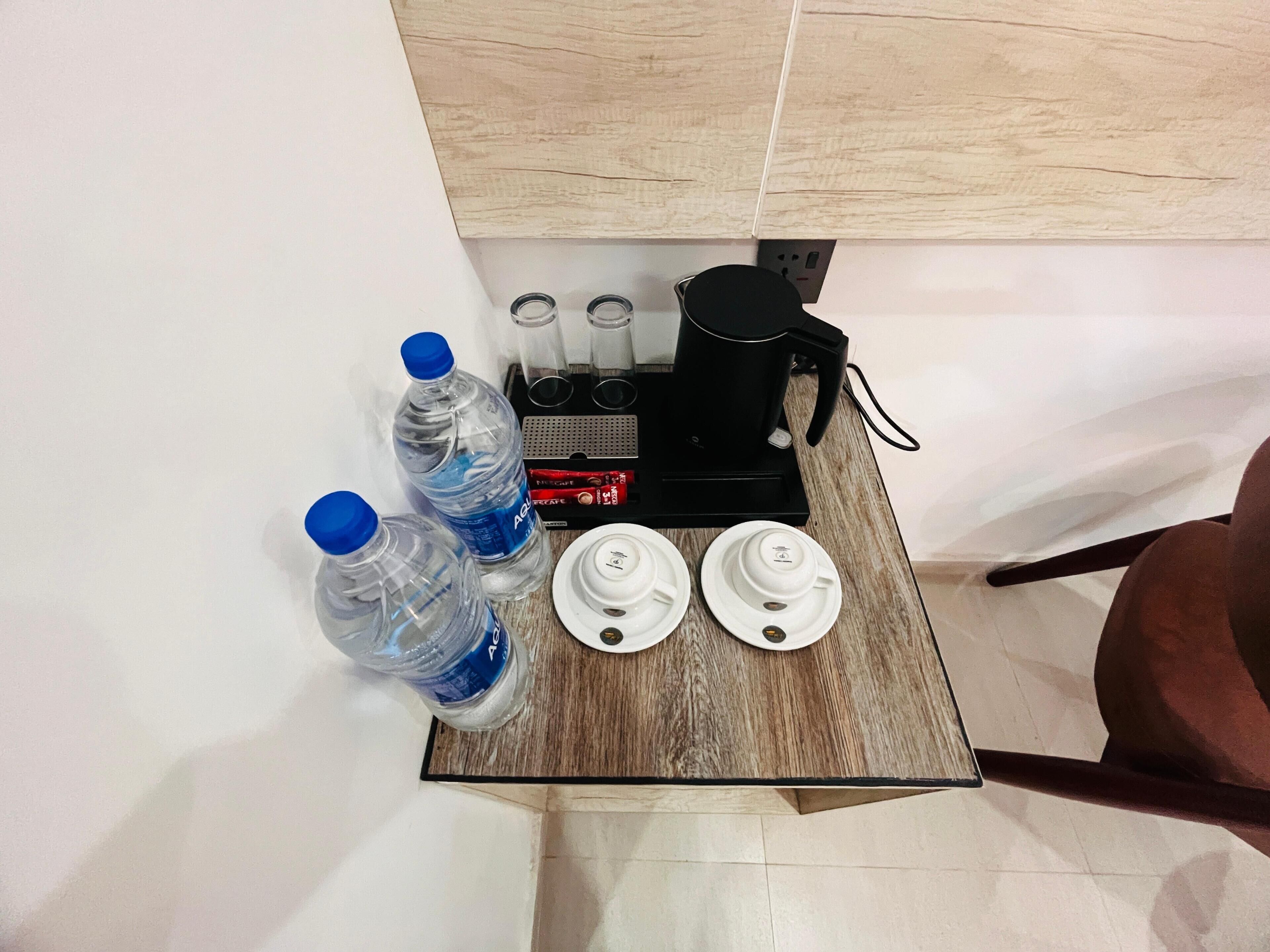 Eine Kaffeemaschine, zwei Wasserflaschen und zwei weiße Tassen auf einem Holztisch.