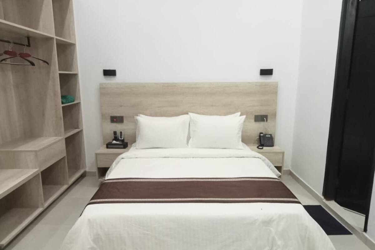 Un dormitorio con cama, armario, mesita de noche y lámpara de pared.