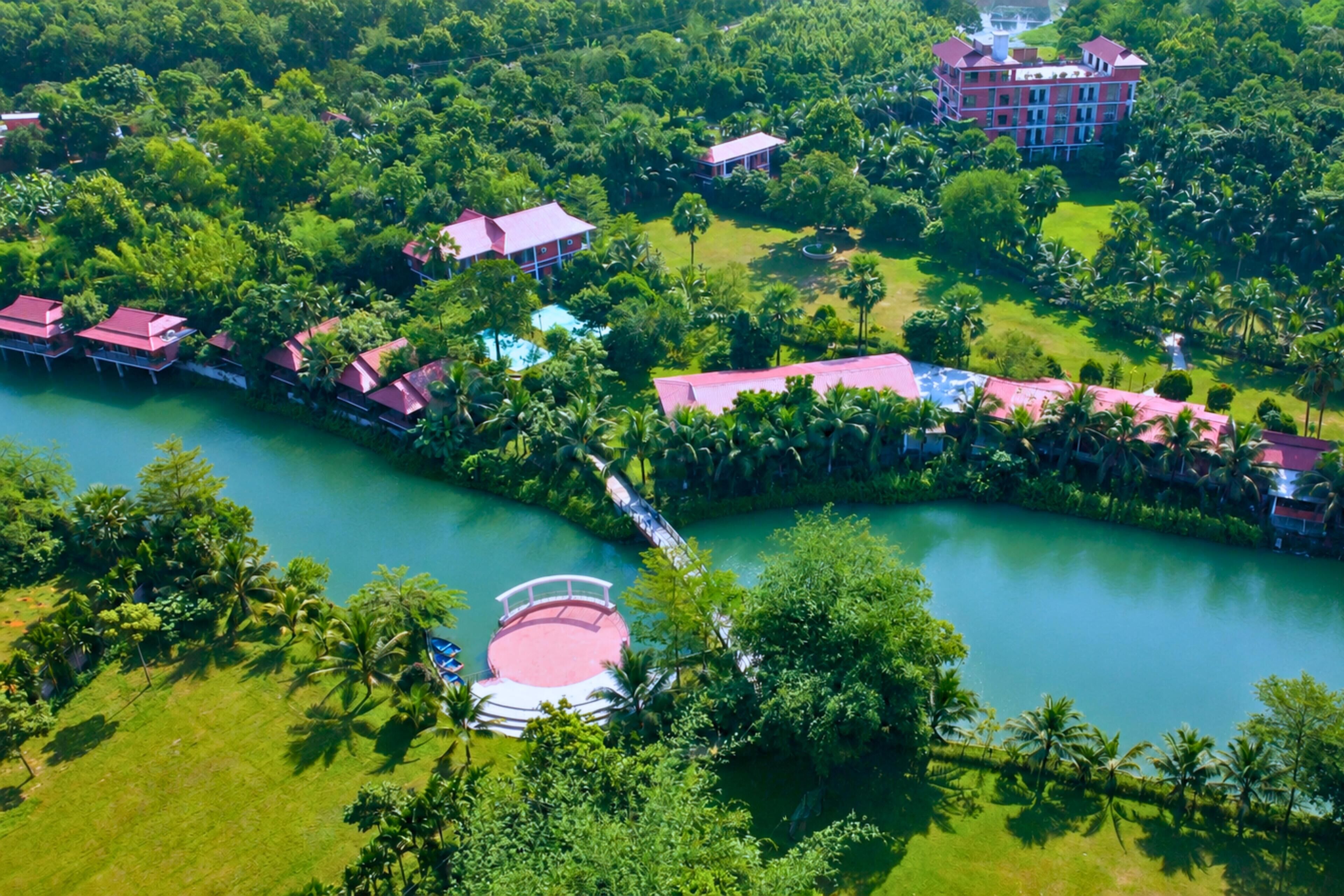 An aerial view of a resort with multiple buildings, a central pool, and lush greenery.
