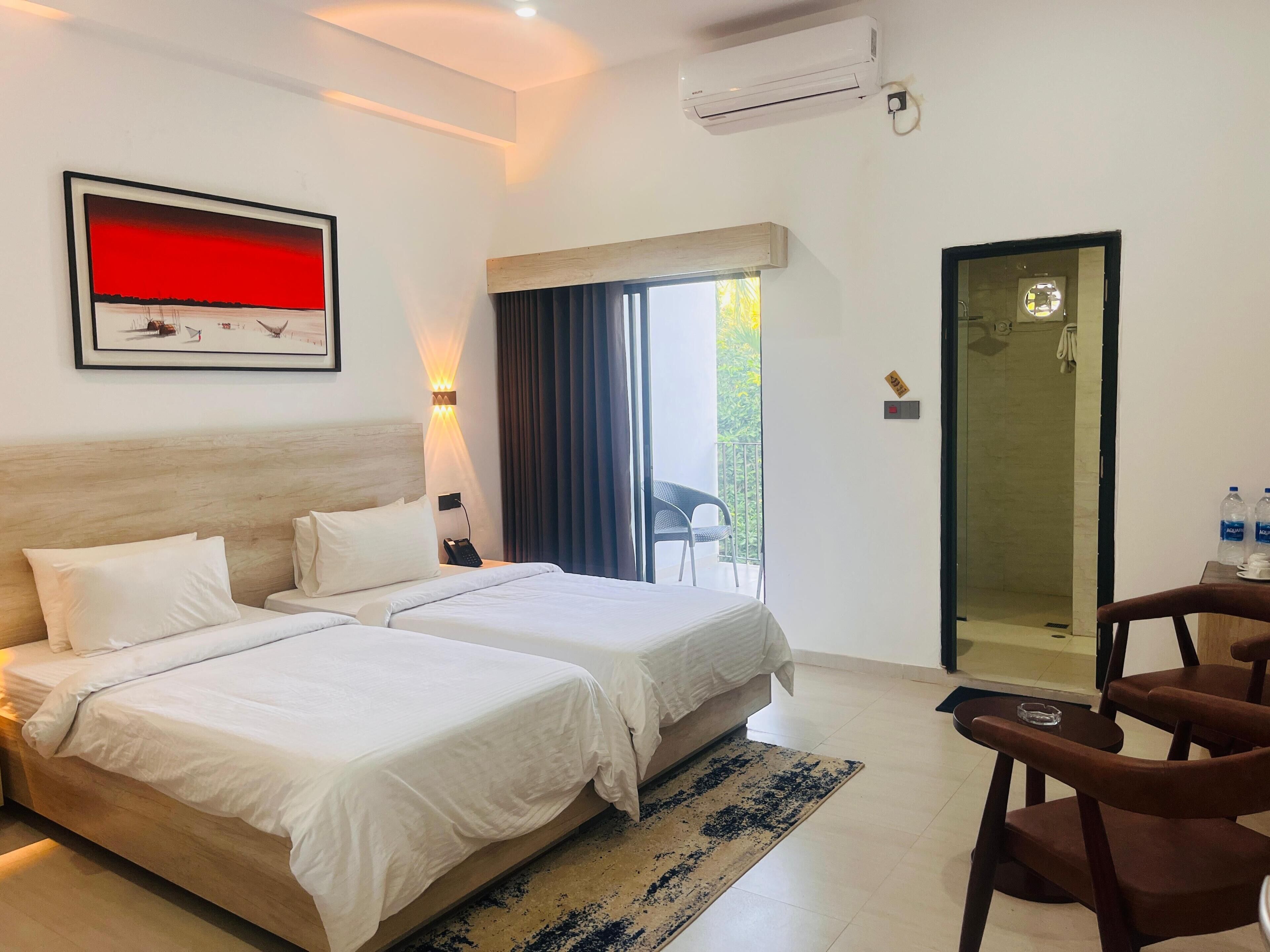 Ein Hotelzimmer mit zwei Betten, einem Schreibtisch, einem Stuhl, einem Badezimmer mit Glastür und einem Balkon mit Blick.
