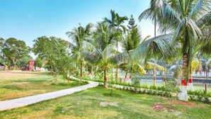 A pathway through a park with palm trees and a red building in the background. - Kokomo Sunset Resort (Sreepur)