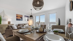 Un espace repas moderne avec une table en bois dressée pour deux personnes, un canapé et un balcon offrant une vue agréable.
