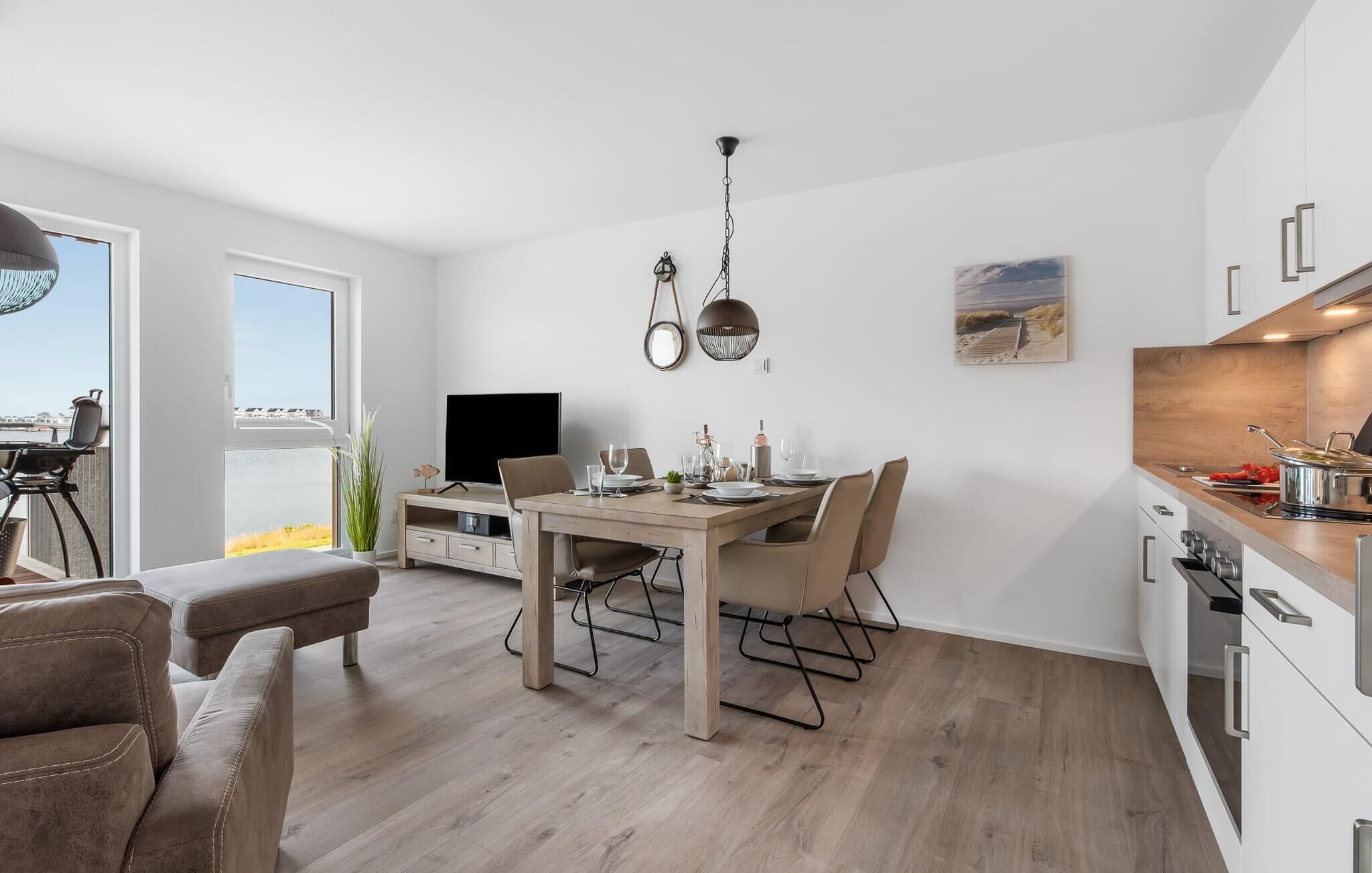 Un salon moderne doté d’une grande fenêtre, un coin repas avec une table et des chaises en bois, un téléviseur et une cuisine équipée d’une cuisinière et de placards.