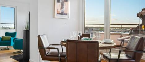A modern living room with a dining area, large windows, and a view of the cityscape.