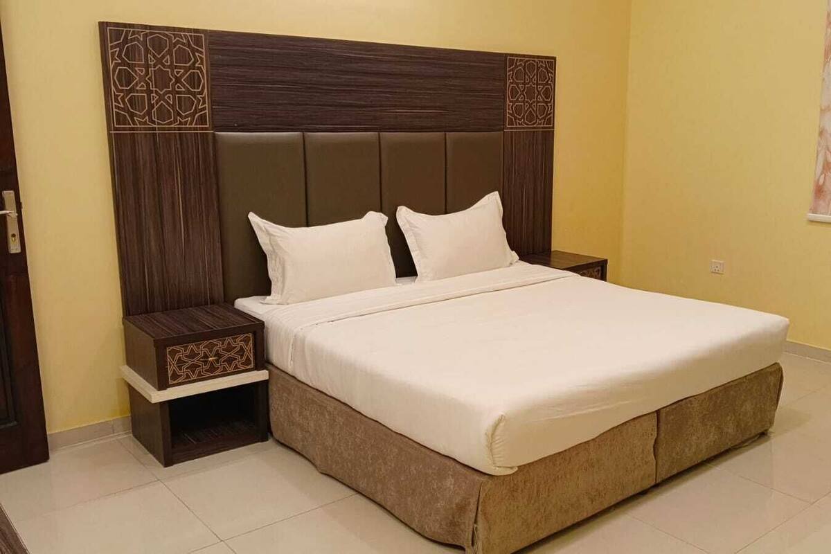 A bedroom with a large bed, two bedside tables, and a headboard with a geometric pattern.