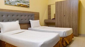 A hotel room with two beds, a grey tufted headboard, a wooden wardrobe, and a painting on the wall. - Wadan Al-Mutamayeza Furnished Apartments (Rabigh)