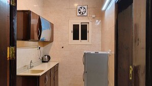 A compact kitchen with a sink, kettle, and a small window. - Wadan Al-Mutamayeza Furnished Apartments (Rabigh)