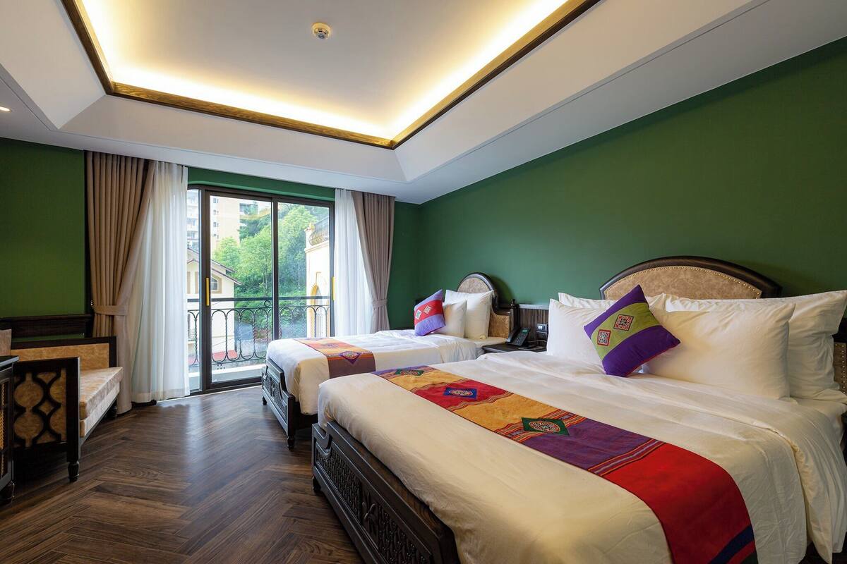 A hotel room with two beds, a wooden floor, a balcony with curtains, and a green wall.