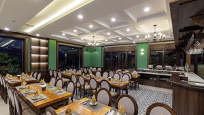 Un comedor amplio con varias mesas y sillas, una estación de servicio central y un candelabro.