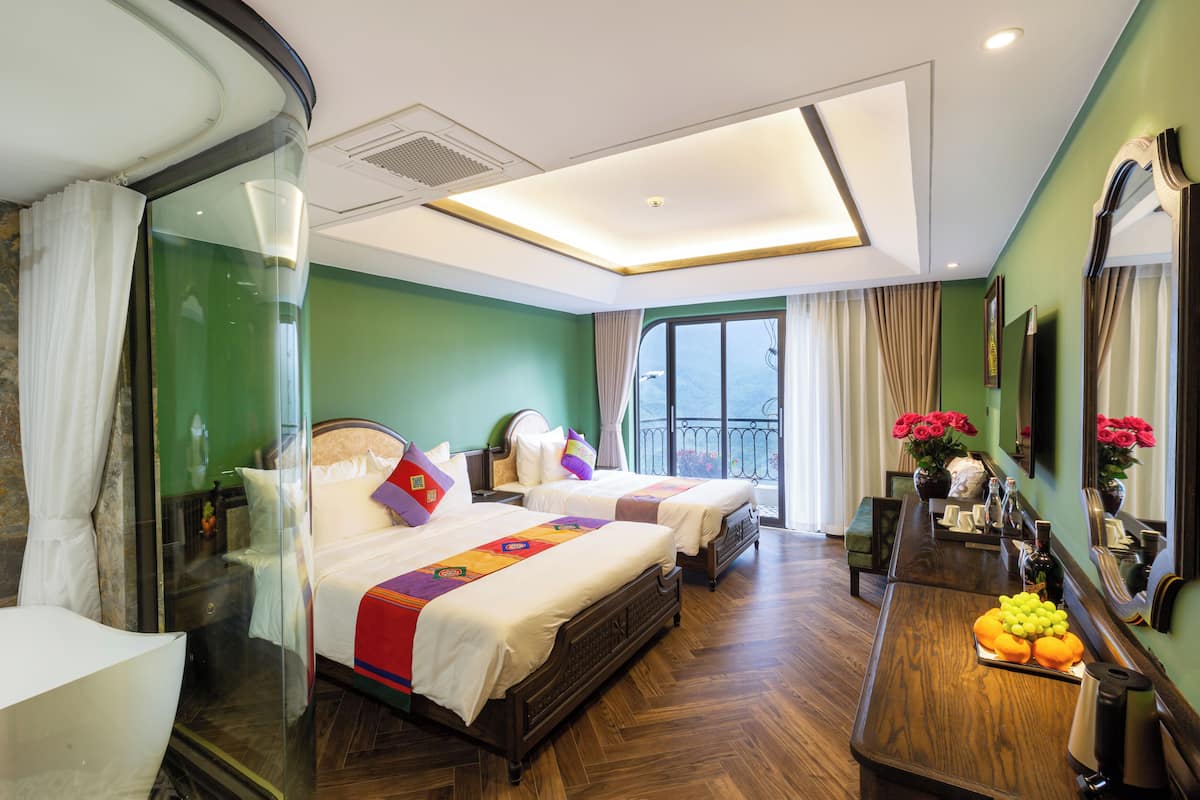 A hotel room with two beds, a wooden desk, a mirror, and a balcony with a view.