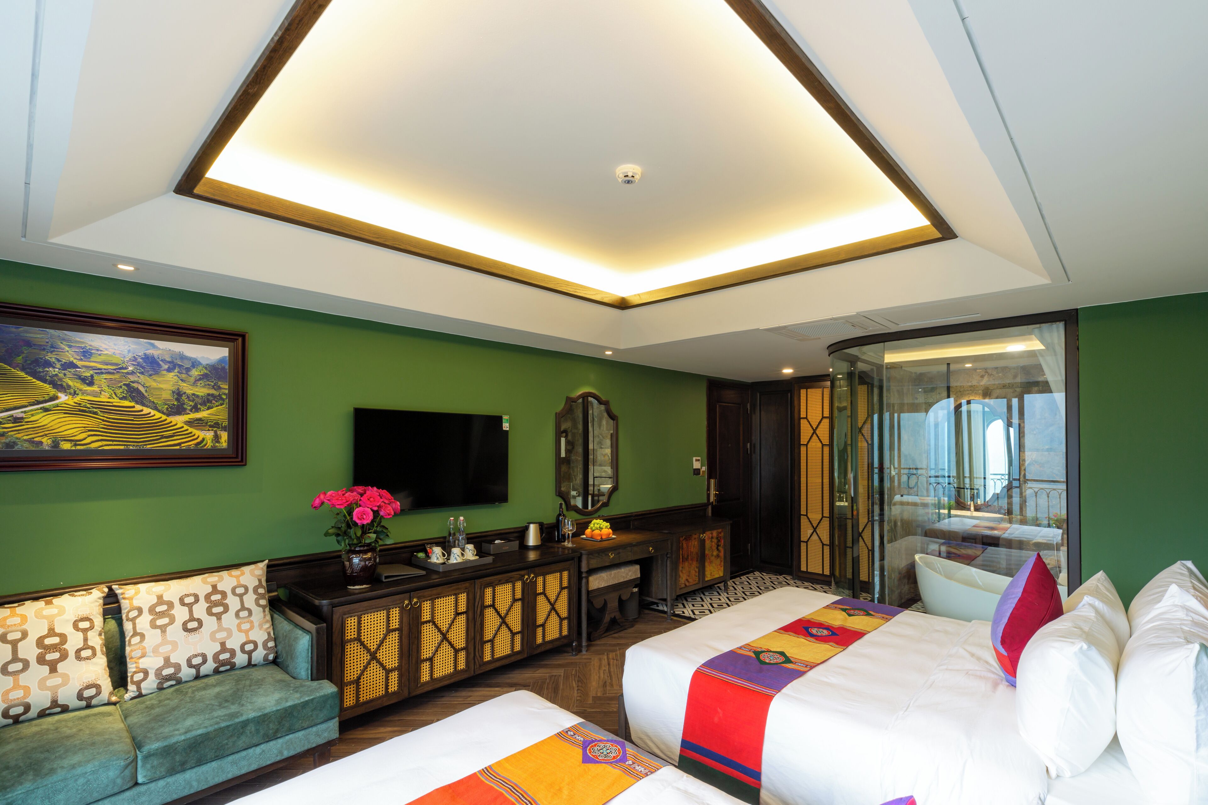 A hotel room with a large bed, a sofa, a TV, a mirror, and a window with a view of a building.