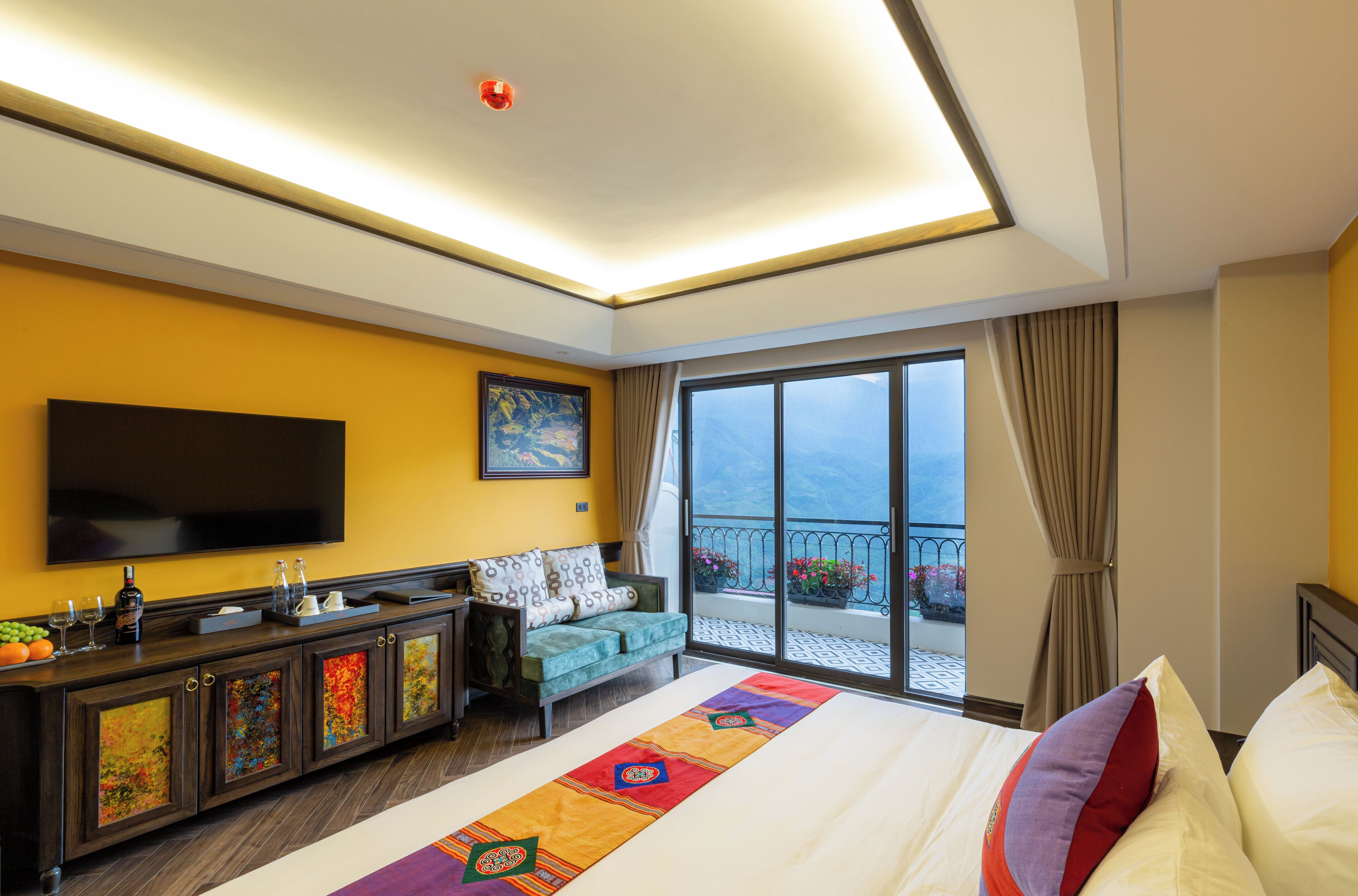 A hotel room with a large bed, a sofa, a TV, a balcony with a view, and a minibar.