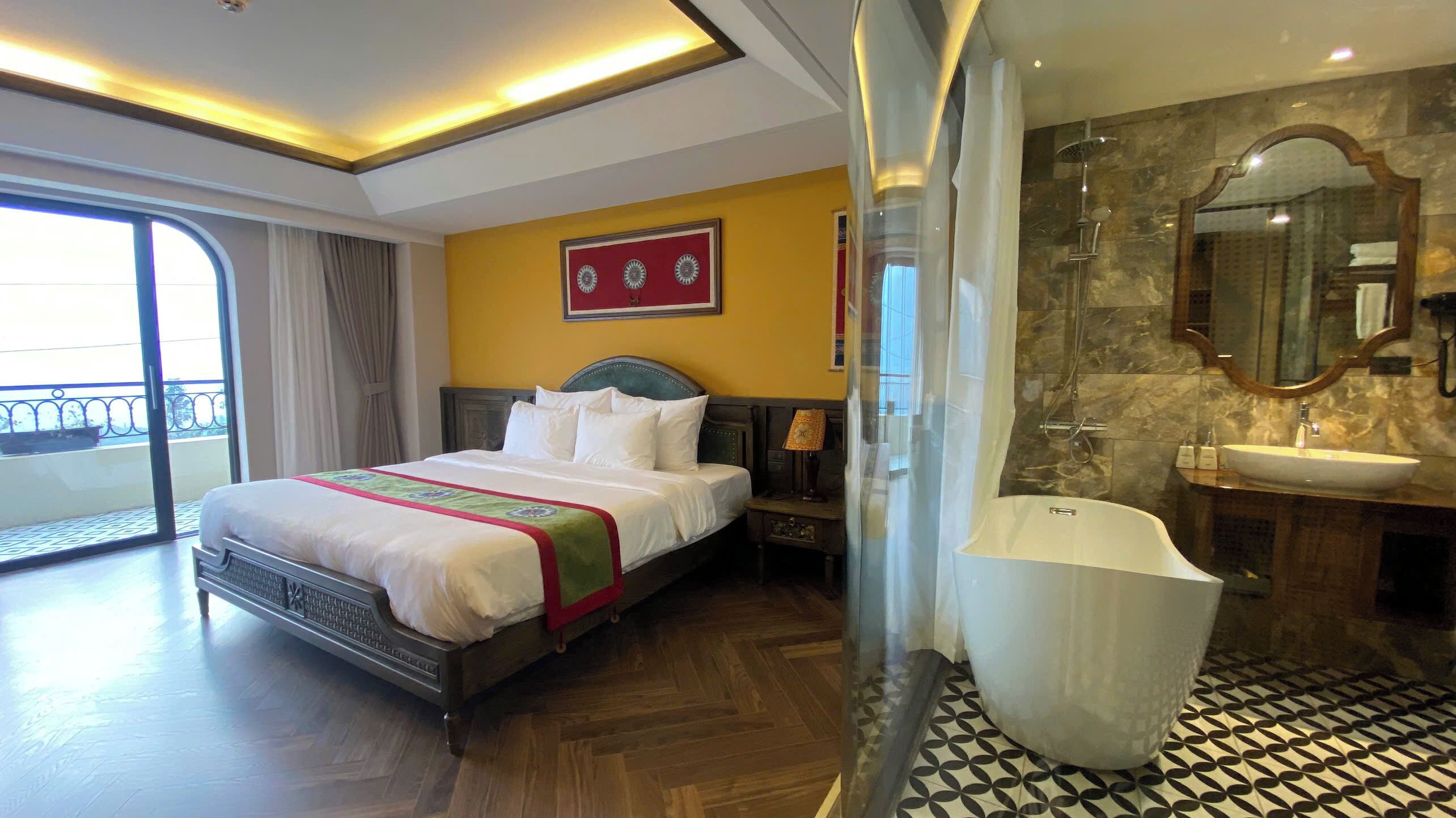 A hotel room with a large bed, a bathroom with a bathtub, and a balcony with a view.